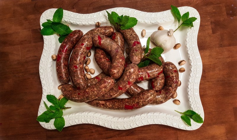 Uncooked Pistachio Pesto Sausages on a white platter with pistachios and mint.